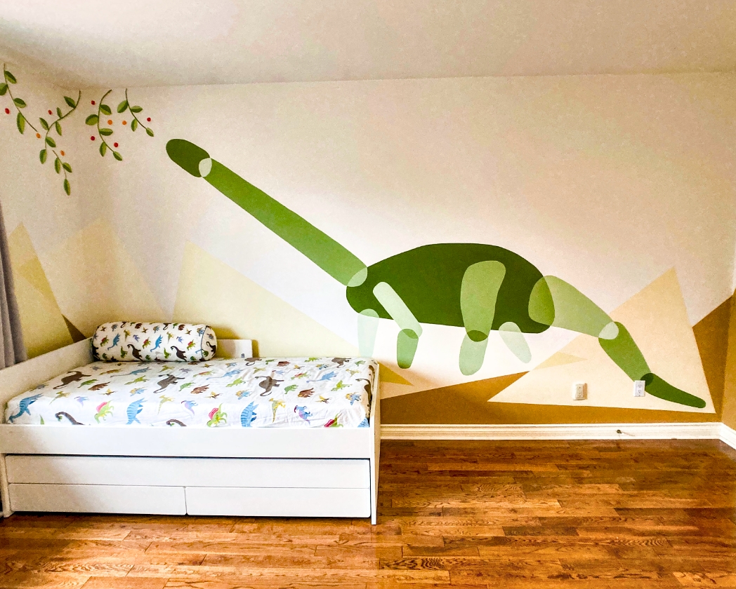Boys' shared bedroom with a custom dinosaur mural featuring a large long-necked sauropod in dark and medium green stretching across the wall, set against abstract mountain shapes in muted gold and cream, with a green leafy branch and red berries in the upper corner, above a white trundle bed dressed in dinosaur-print bedding and a matching bolster pillow, with light hardwood floor