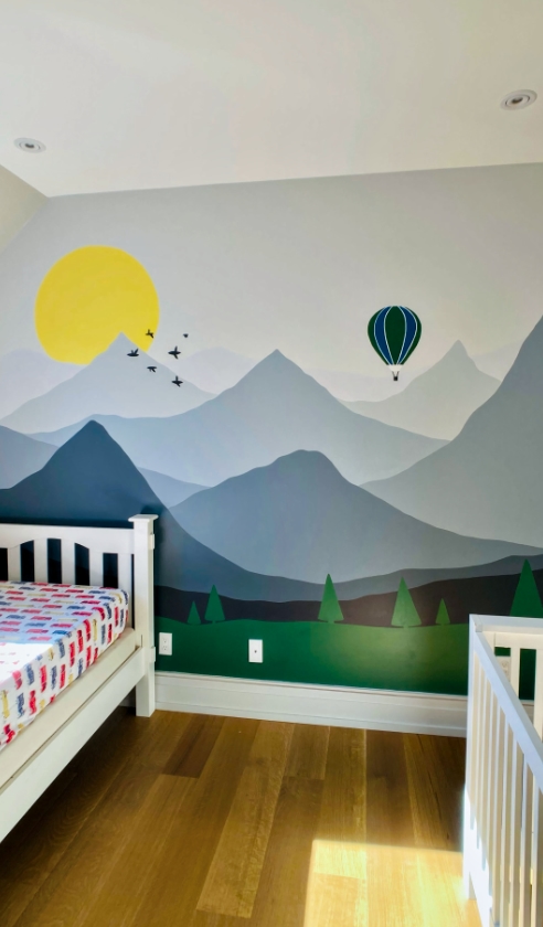 Misty mountain landscape mural in kids' bedroom with layered peaks, sun, hot air balloon, and pine trees