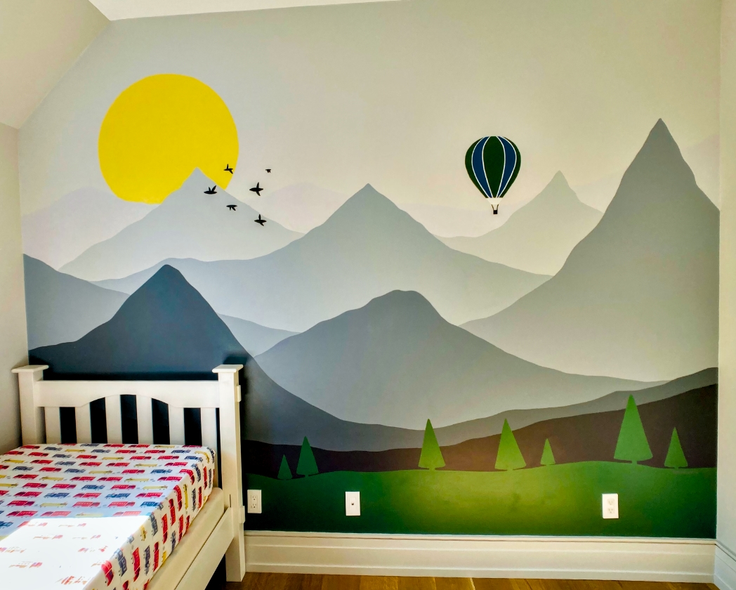 Misty mountains mural wide view with yellow sun, flying birds, hot air balloon, layered peaks, and pine forest in kids' bedroom