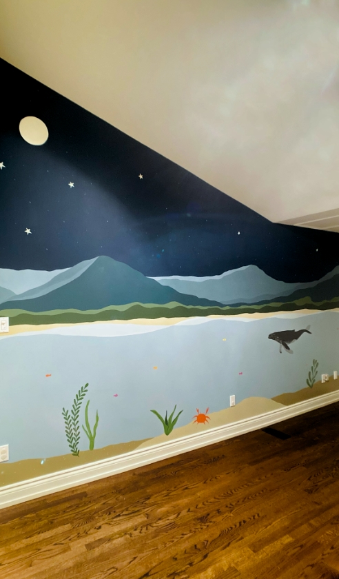 Ocean and night sky mural in kids' room with whale, starry sky, moon, mountains, and underwater scene with seaweed and crab