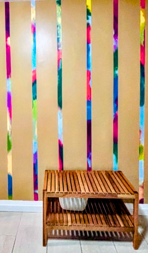 Colorful watercolor stripes mural painted on mudroom accent wall with wooden bench and storage chest.