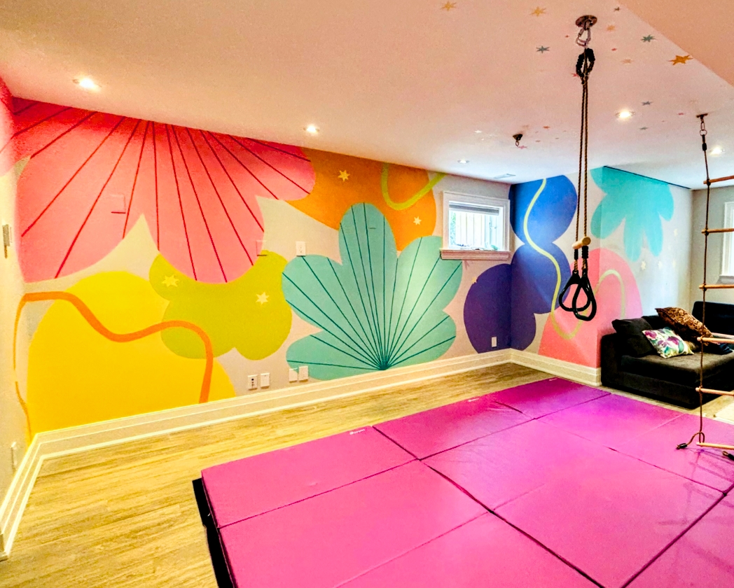 Kids' playroom with a hand-painted tropical floral mural featuring a large red flower, oversized yellow and teal leaf shapes, purple and blue abstract florals, colourful stars on the ceiling, gymnastics rings, a rope ladder, and a pink foam mat