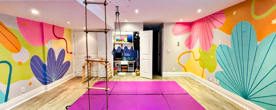 Vibrant tropical floral playroom mural with pink, purple, and teal botanicals, climbing rope, and pink gymnastics mat